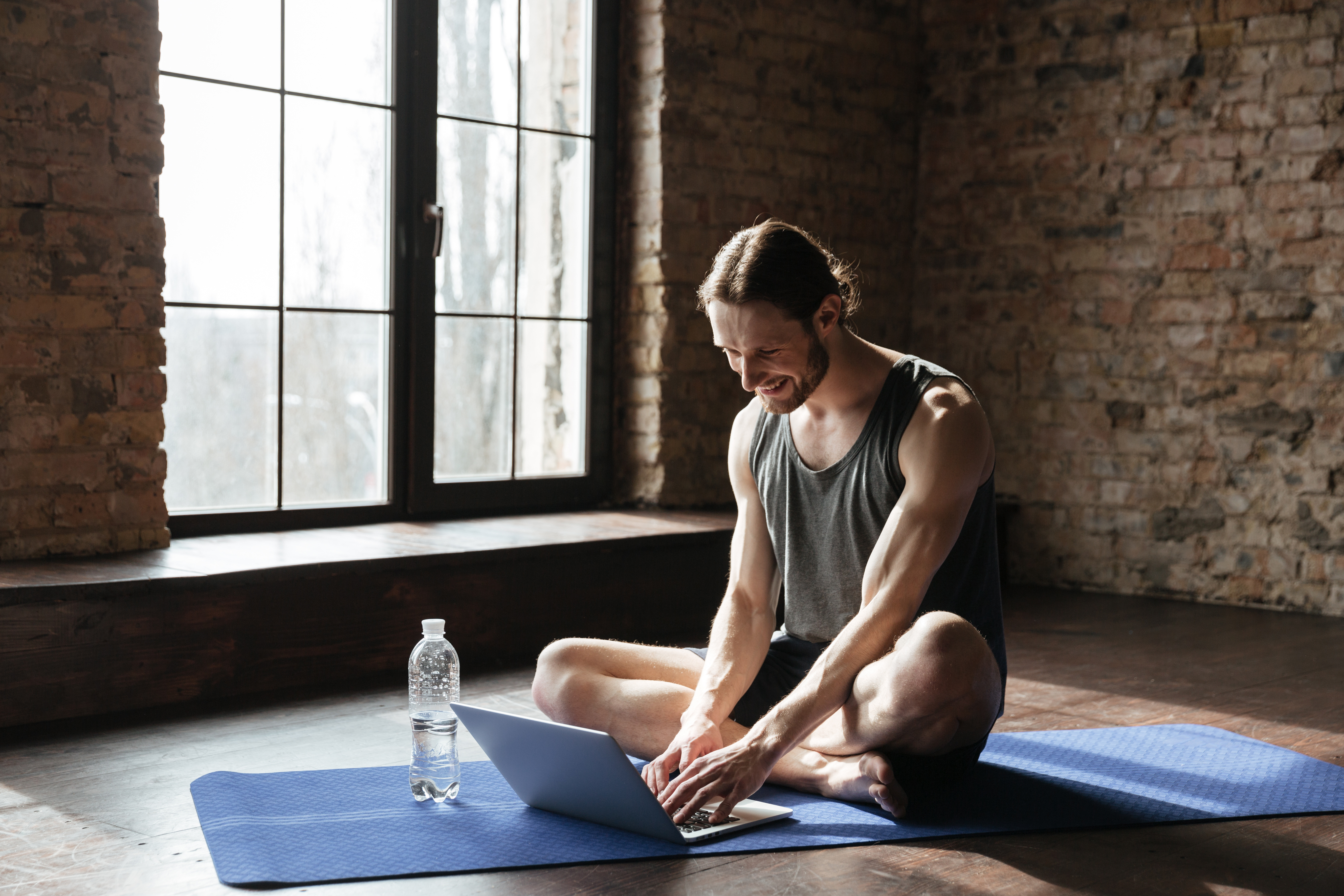 handsome-strong-sportsman-sitting-near-bottle-water-using-laptop