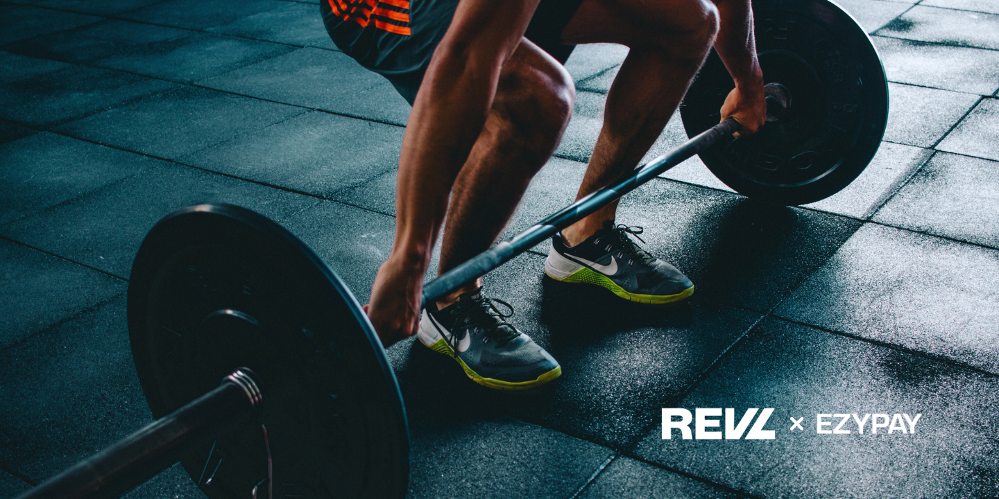 A person squatting, about to lift a large weight. They are wearing trainers. Beside the image, two logos sit: one for Ezypay and one for REVL training